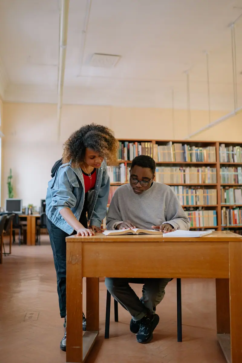 Voksne som studerer sammen ved et bord i et bibliotek med bokhyller i bakgrunnen